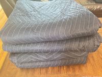 Three folded navy blue quilted moving blankets stacked on table