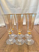 Front angled view of all six amber tinted champagne flutes standing on wooden surface