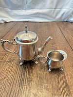 Front view of silver-plated teapot and creamer on wood surface