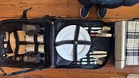 Backpack open showing plates, cutlery, mugs, wine glasses, cutting board, corkscrew, napkin and flask