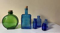 All six colored glass bottles arranged in a row showing shapes, colors and stoppers