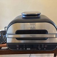 Front and top view of Ninja air fryer countertop oven showing stainless and black finish, power cord and control panel