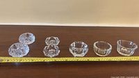 Seven clear pressed glass salt cellars aligned on table with tape measure for scale