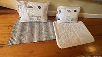 Two sealed pillows and two bath mats displayed on floor