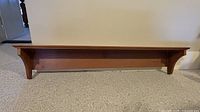Front view of wooden wall shelf showing top board and side brackets