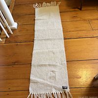 Full view of cream fringed scarf on wooden floor