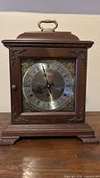 Front view showing wood case, glass door, dial with Roman numerals and brass spandrels