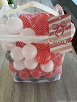Mesh bag of red, white, black ball pit balls with brand tag visible