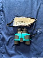 Front view of turquoise Tasco binoculars with strap and pamphlet on blue fabric