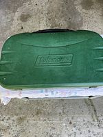 Closed green Coleman stove with embossed logo and carry handle