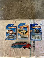 Overview of three carded Hot Wheels cars plus loose red cab and blue trailer