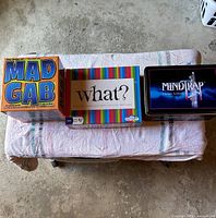 Front view of all three game boxes: Mad Gab, What?, MindTrap Classic Edition