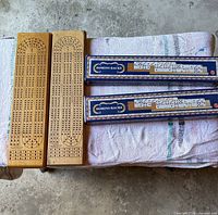 Two wooden cribbage boards alongside two boxed Domino Racks sets on table