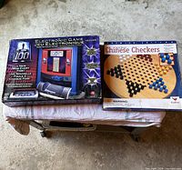 Front view of two boxed games on stool: Chinese Checkers and electronic trivia game packaging visible