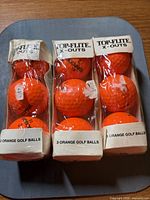 Front view showing three unopened sleeves of orange Spalding Top-Flite X-Out golf balls