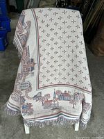 Full view of woven throw draped to show village scene, border, and fringe