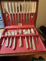 Open wood chest showing knives in lid, assorted spoons and forks in base