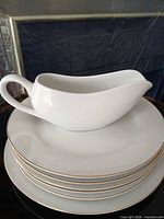 Stack of white plates with gold rims topped by matching gravy boat