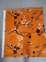 Folded section of orange fabric showing full bird and floral print