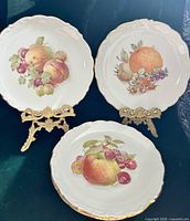 Three of the plates showing fruit motifs and gold-trimmed scalloped rims