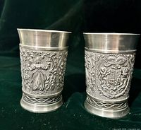 Front view of two SKS Zinn pewter cups showing relief figures and coat of arms