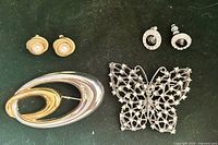 Group shot of two brooches and two pairs of earrings on dark background