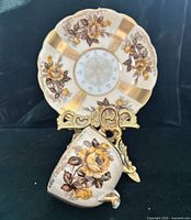 Teacup resting against saucer on stand showing rose pattern and gold bands