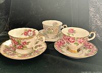 Front view of three teacup and saucer sets showing floral patterns and gold accents
