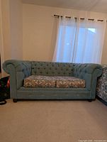 Front view of blue tufted love seat with patterned cushions
