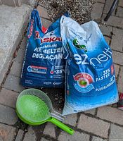 Two ice melt bags and green scoop on driveway