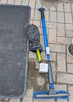 Mat, snow brush, and scraper mitt laid on pavement