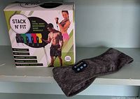 Retail box of Stack N' Fit resistance band set next to Bluetooth headband