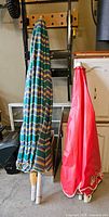Two closed patio umbrellas leaning against wall; left multicolour striped, right red Grand Marnier logo