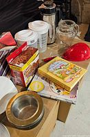 Overview of baking and kitchen items including pitchers, carafe, glass pitcher, colander, cookbooks, boxed brownie pan, baking rings, bowl and peeler