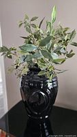 Black ceramic vase containing artificial seeded eucalyptus