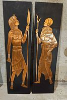Pair of black wood plaques each with applied copper relief Egyptian figures