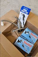 Open box showing chrome faucet and three boxed Shattaf sprayer kits