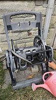 Front view of grey hose reel cart showing handle, drum, attached leader hose, watering can visible