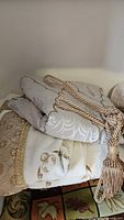 Folded ivory and beige jacquard linens with gold rope tassel tieback