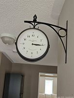 Full view of clock mounted on wall showing bracket, clock faces, finial and surrounding area