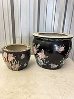 Large and small black ceramic floral planters side by side