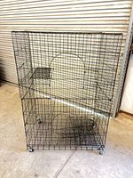 Front view of entire black metal wire bird cage showing size, doors, wheels