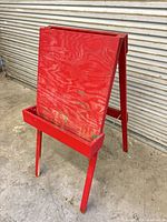 Front view of red wooden children’s easel showing tray and paint drips