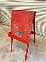 Front view of red wooden easel showing paint-splattered board and built-in tray