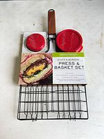 Front view of Stuff-A-Burger press and basket set in packaging, showing wooden handle, red press lids, product image