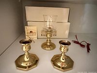 three brass Baldwin candle holders including two matching candlesticks and one hurricane holder, with boxes behind