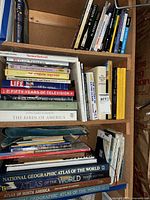 Three shelves packed with large atlases, coffee table and reference books