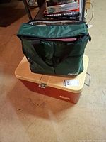 Green Coleman soft sided cooler bag on top of red-orange hard cooler