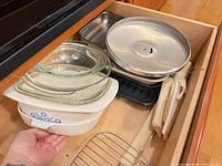 Drawer view showing CorningWare casserole, Pyrex glass dish, round metal lids, black broiler pan base and rack