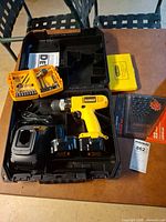 Open carrying case showing drill, charger, batteries, accessory cases, sealed drill-bit set
